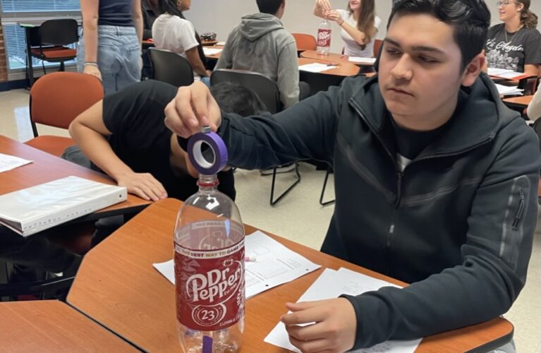 student balances tape on soda bottle