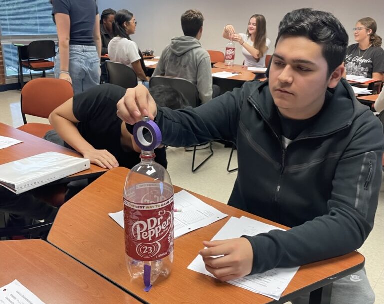 student balances tape on soda bottle